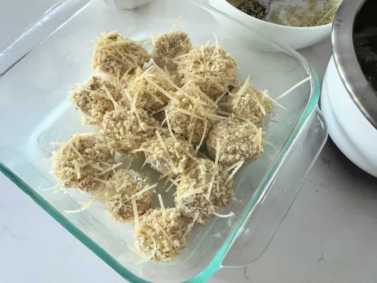 Square glass baking dish filled with breading and parmesan strands stuffed in mushrooms.