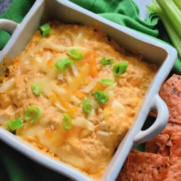Square ceramic bowl filled with orange dip with melted cheese and green onions on it.