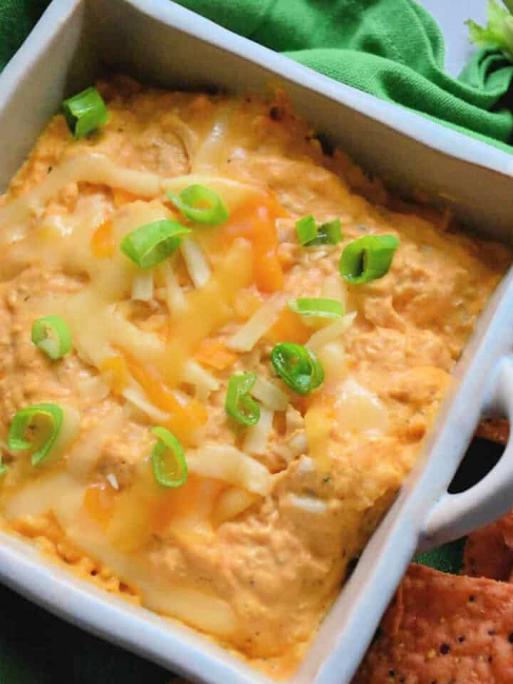 Square ceramic bowl filled with orange dip with melted cheese and green onions on it.