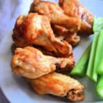 6 chicken wings on a white plate stacked next to celery slices.