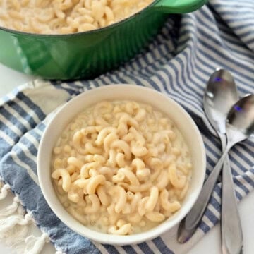 white bowl filled with elbow mac and cheese with two spoons laying on top of striped cloth.