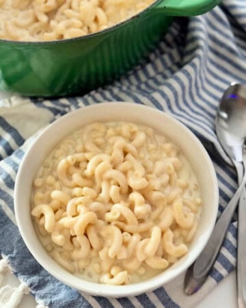 white bowl filled with elbow mac and cheese with two spoons laying on top of striped cloth.