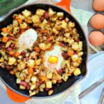 Orange cast iron skillet with potatoes, corned beef, and eggs.