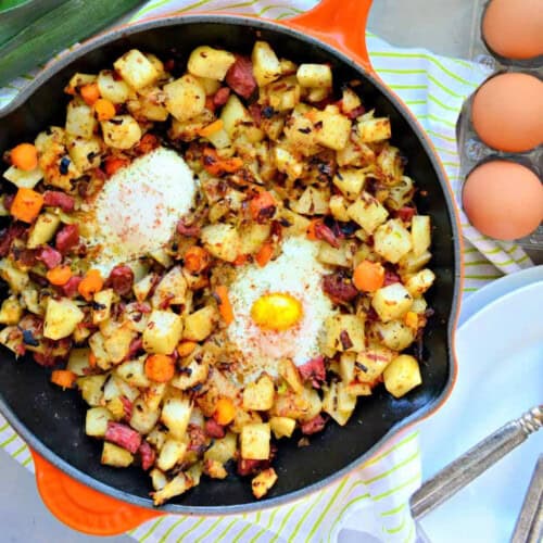 Orange cast iron skillet with potatoes, corned beef, and eggs.
