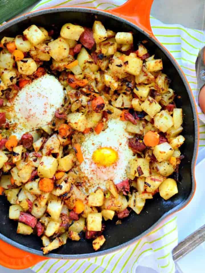 Orange cast iron skillet with potatoes, corned beef, and eggs.