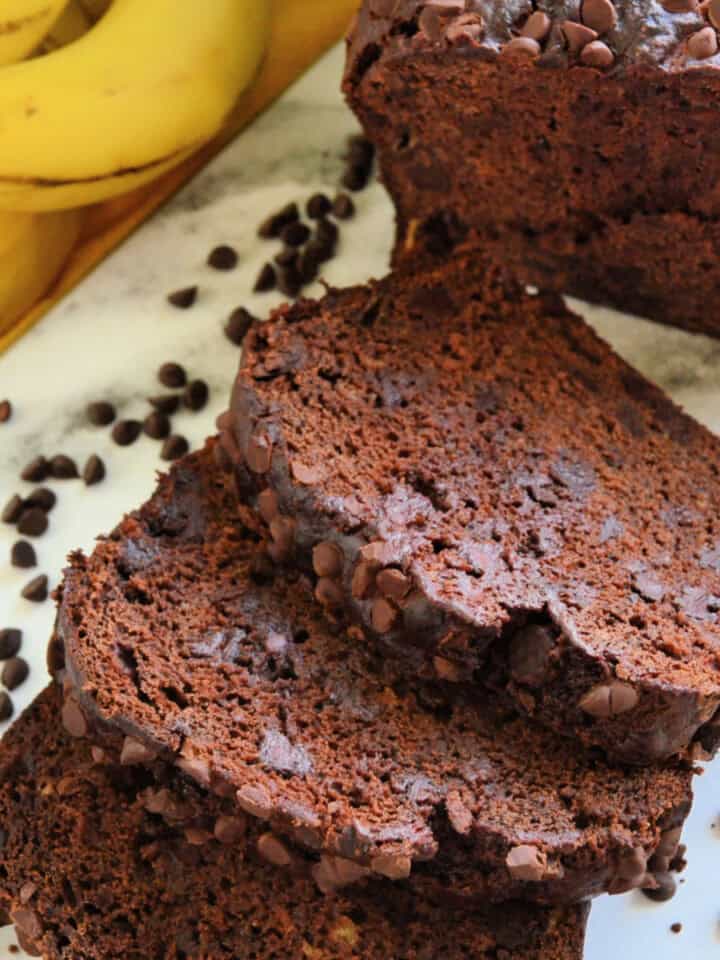 3 slices of chocolate bread on a marble cutting board with a loaf behind it.