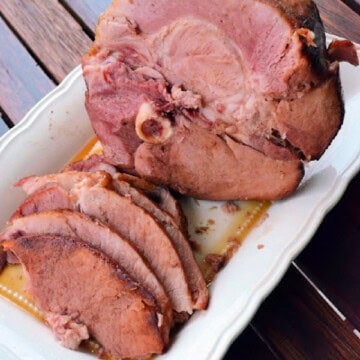 Close up of a whole ham with slices of ham on a white platter.