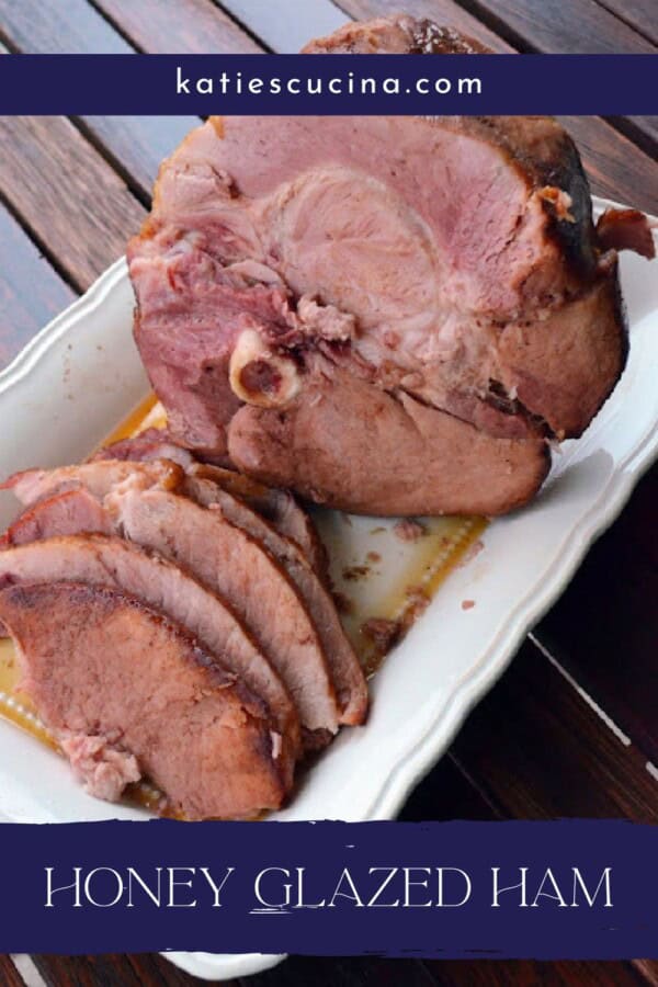 Whole ham with a few slice on a white plate with text on image for pinterest.
