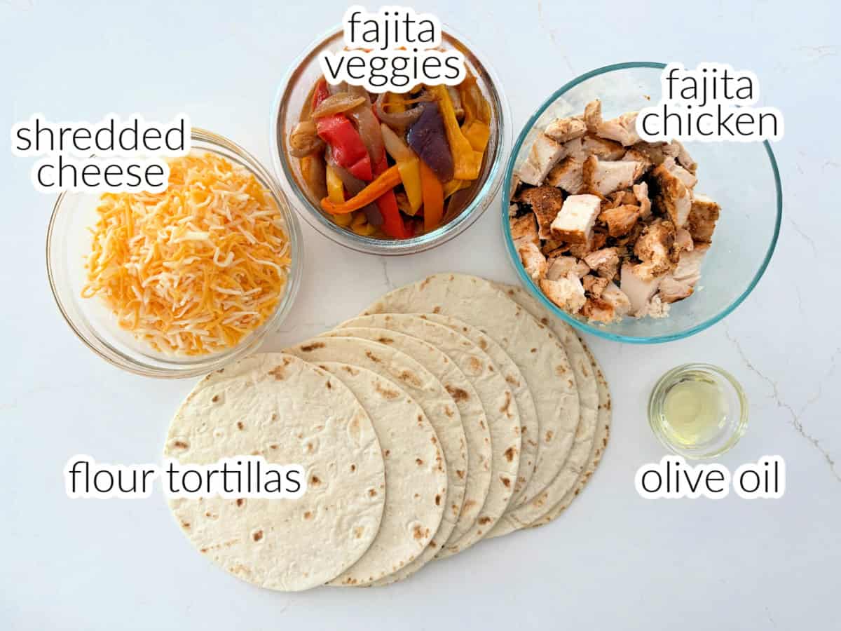 Ingredients on white counter; tortillas, cheese, fajita veggies and chicken, and olive oil.