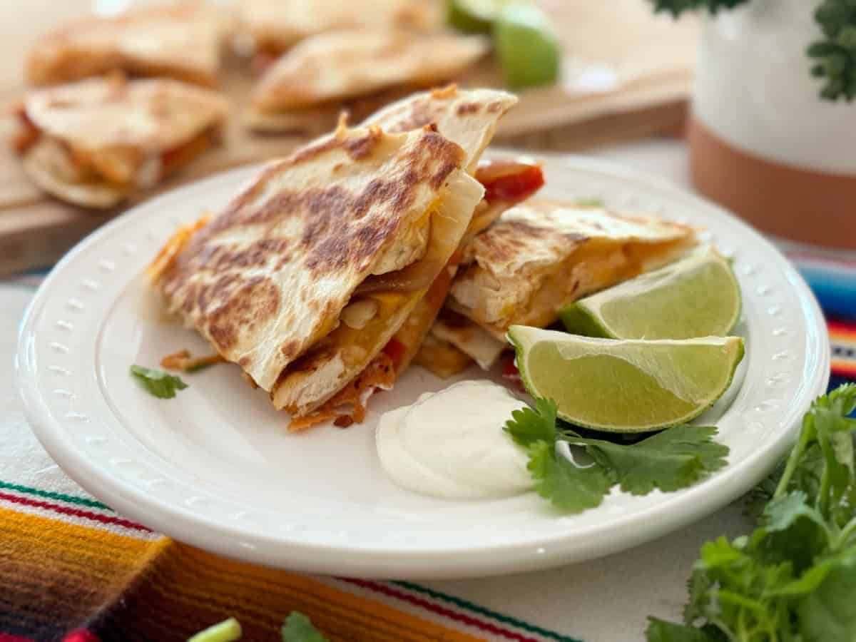 3 slices of quesadillas with lime wedges and sour cream.