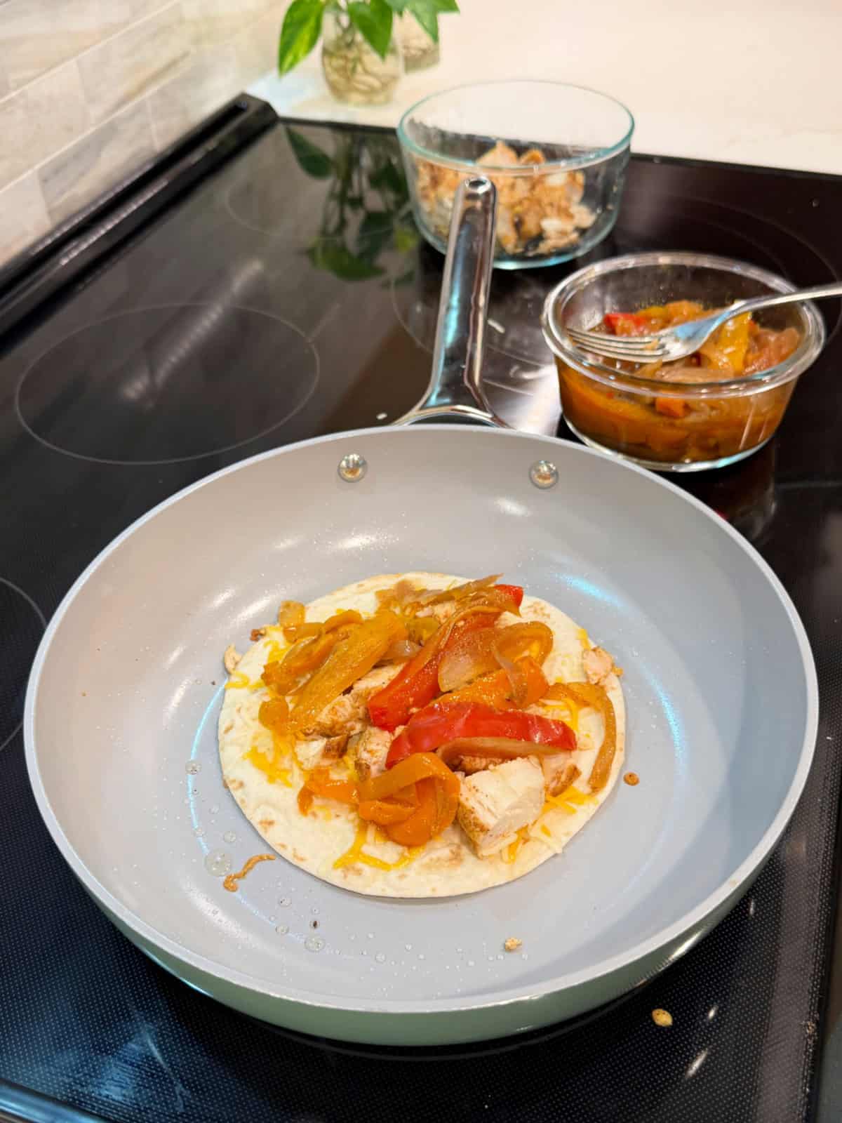 Frying pan filled with a tortilla with cheese, chicken, and peppers on a stove top.