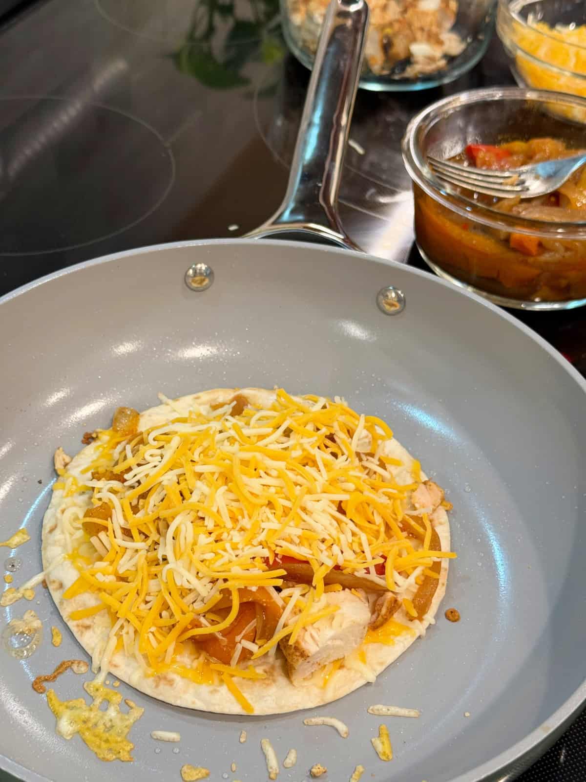 Frying pan filled with flour tortilla with meat, veggies, and cheese.