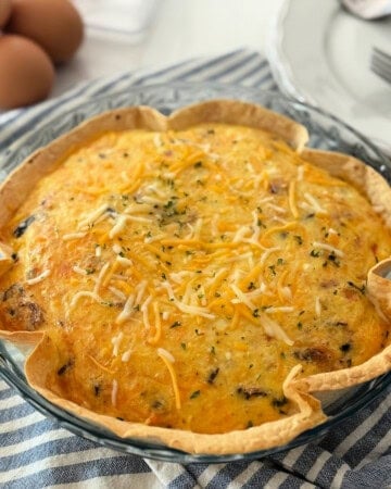 Browned tortilla in a glass pie plate filled with a baked egg and cheese on a blue and white striped cloth.