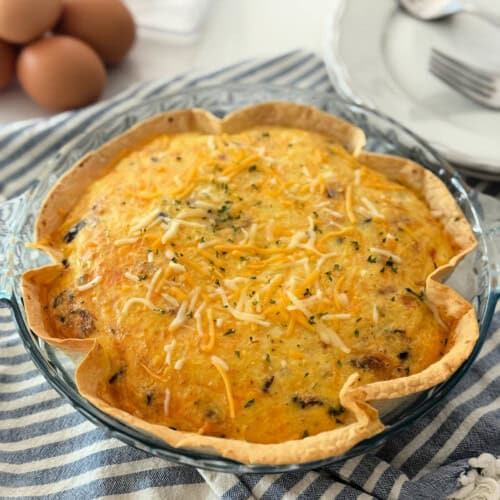Browned tortilla in a glass pie plate filled with a baked egg and cheese on a blue and white striped cloth.