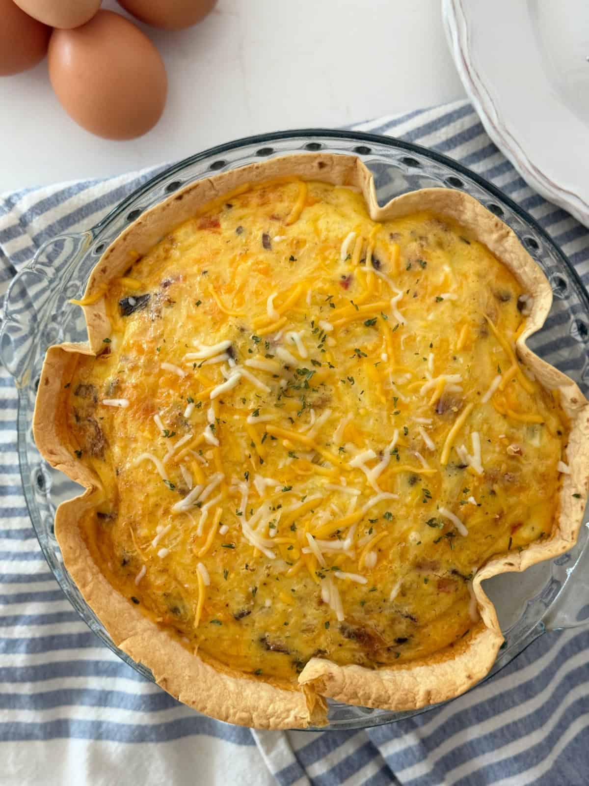Glass pie plate filled with a cooked tortilla and egg baked in it resting on a blue and white striped cloth.