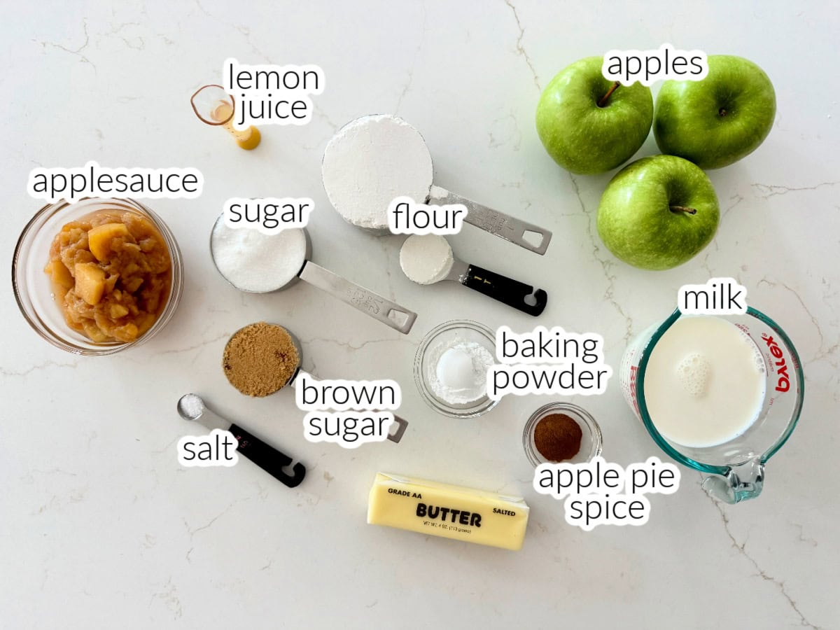 Ingredients on counter; apples, lemon juice, applesauce, flour, butter, milk, sugar, salt, apple pie spice, and baking powder.