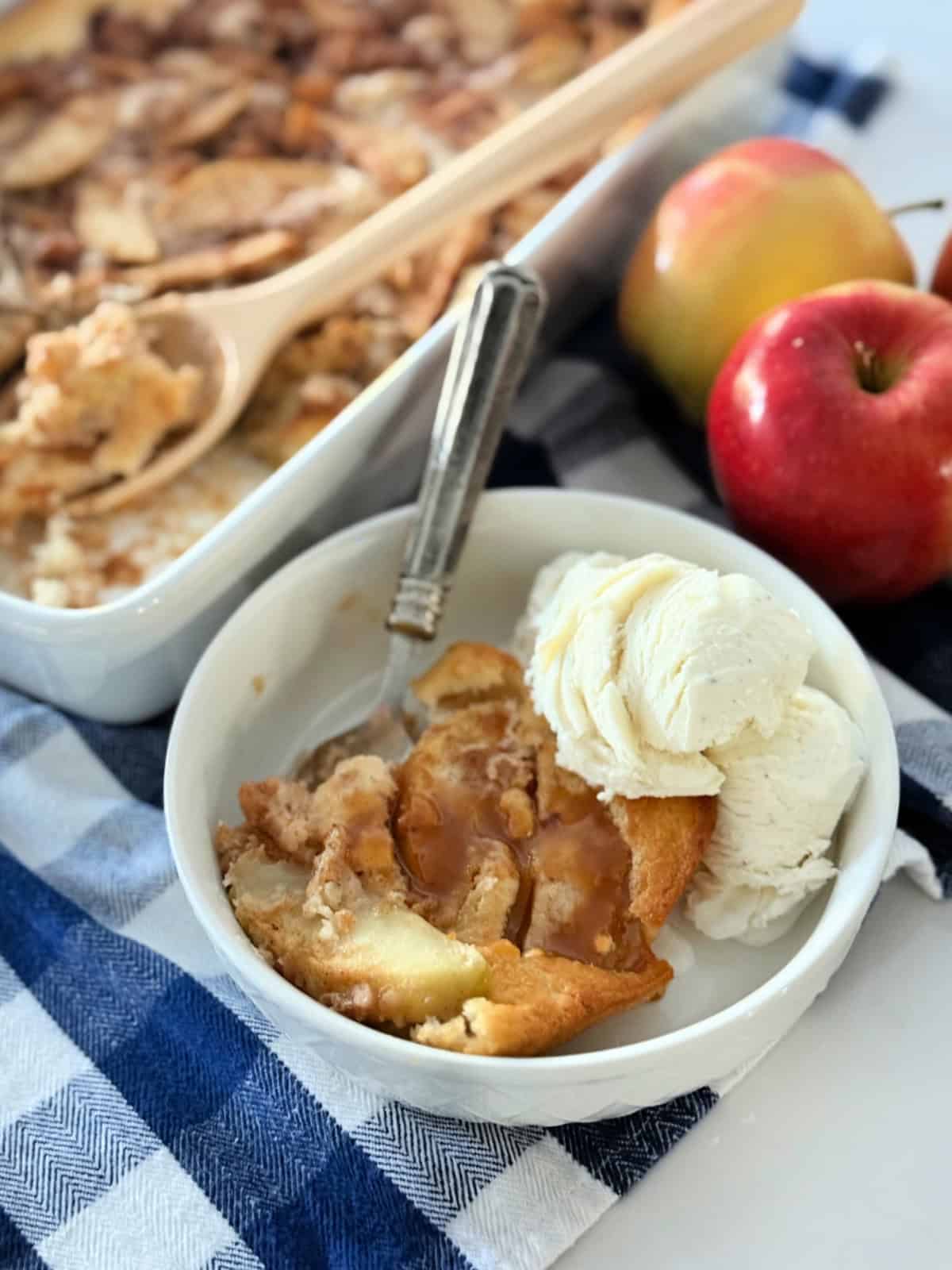 White bowl filled with apple cobbler and ice cream sitting on a blue and white checkered cloth.