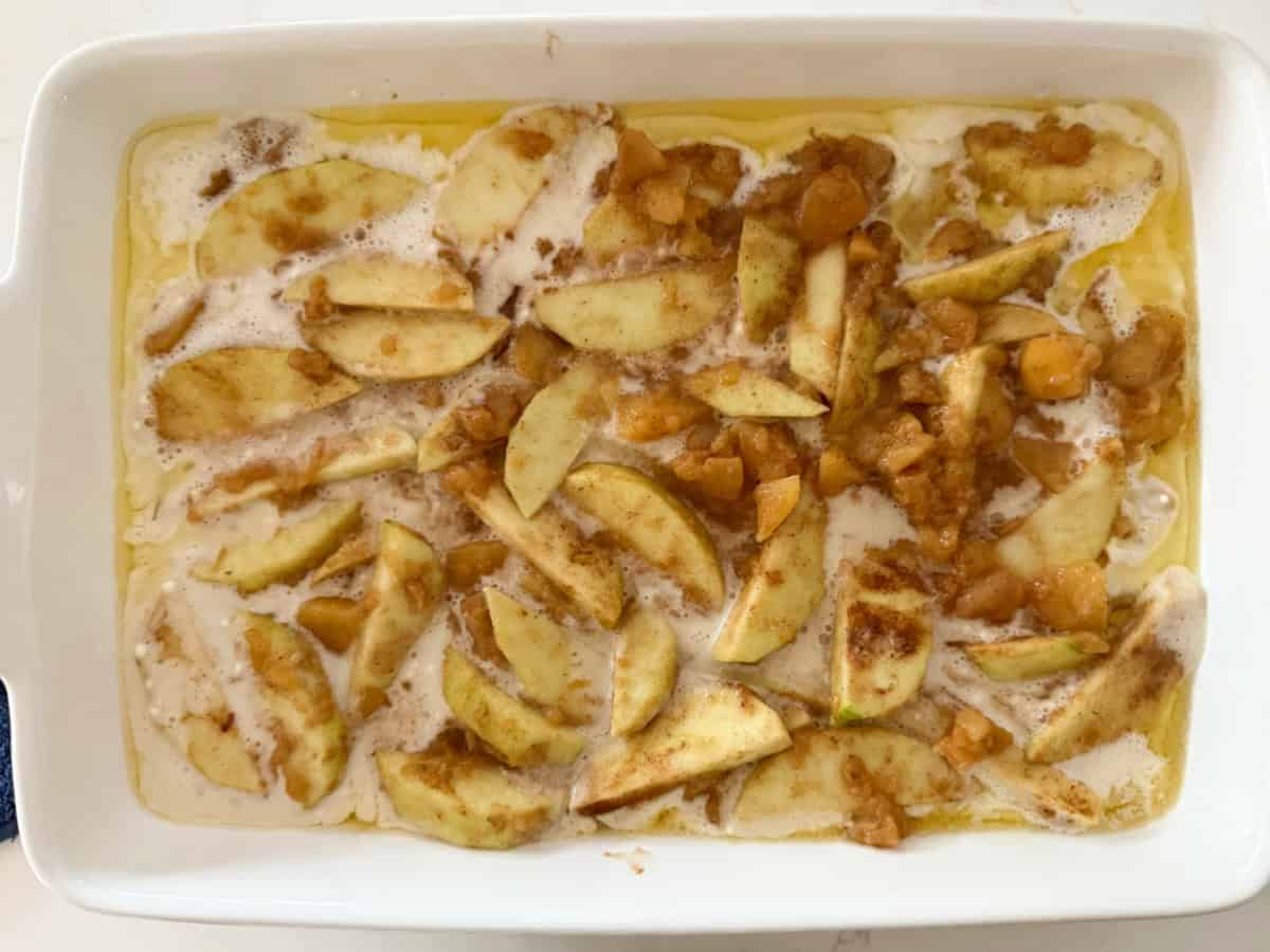 White baking dish filled with batter, butter, and cinnamon coated apples.