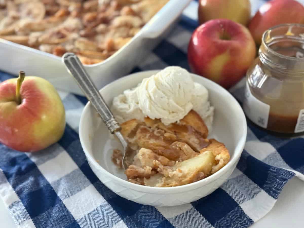 White bowl filled with apple cobbler, ice cream and cobbler in the background.