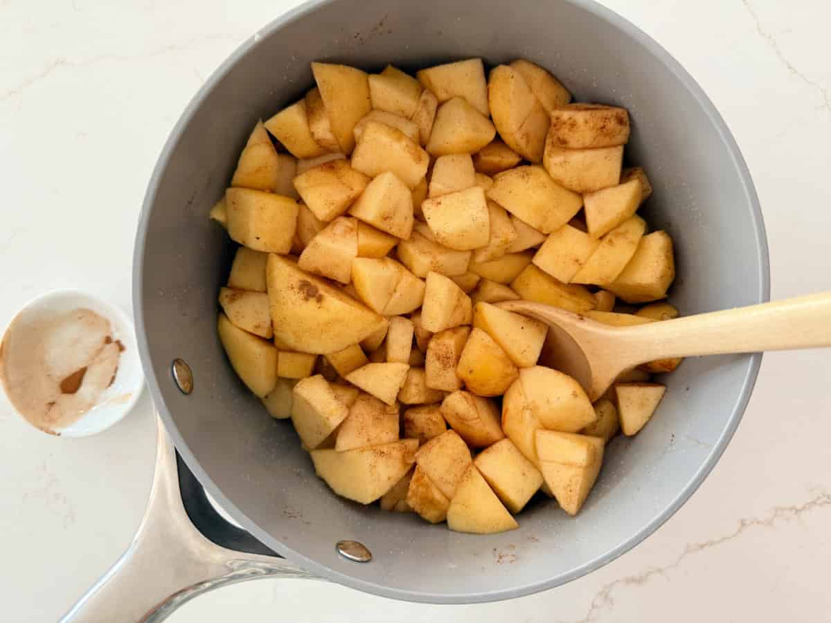 Diced apples coated in cinnamon in a sauce pot on a white countertop.