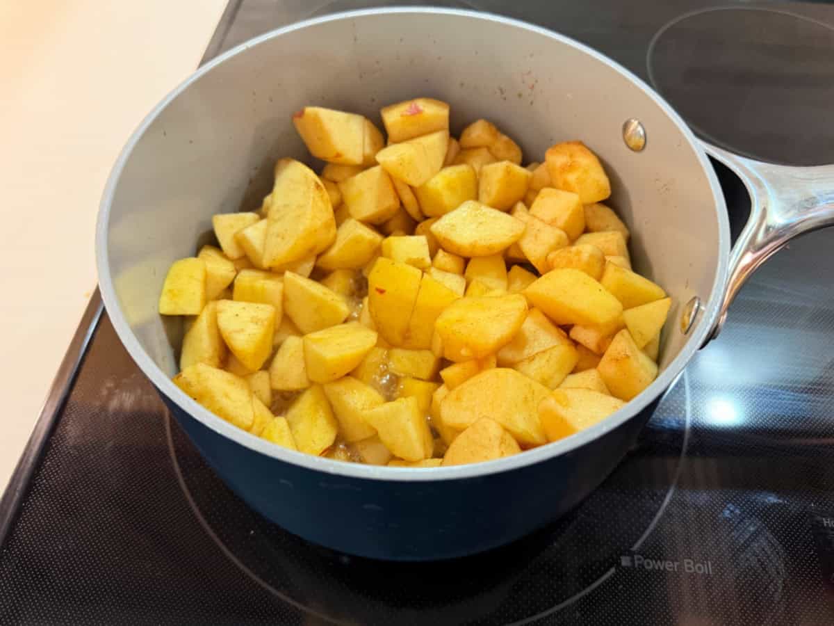 Diced apples in a blue sauce pot on a black stove top.