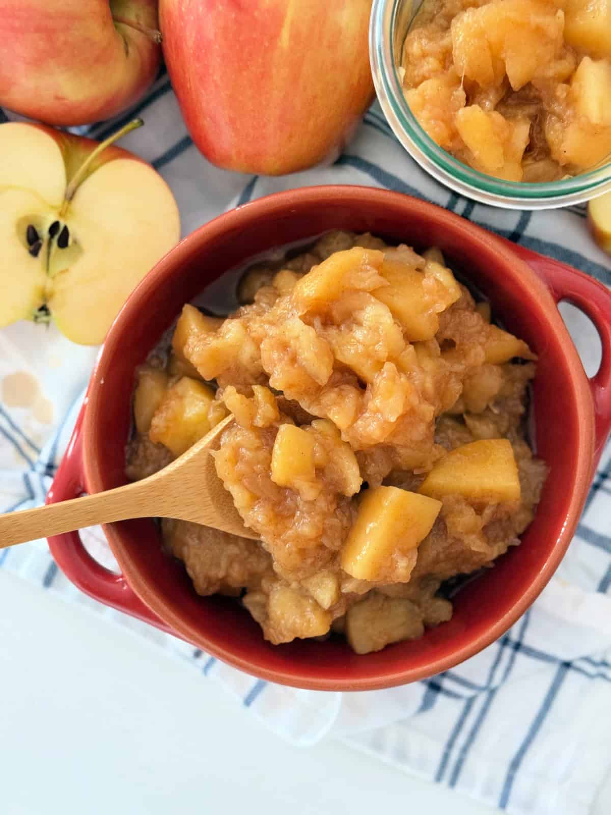 Red bowl filled with applesauce next to fresh apples and a jar of applesauce.
