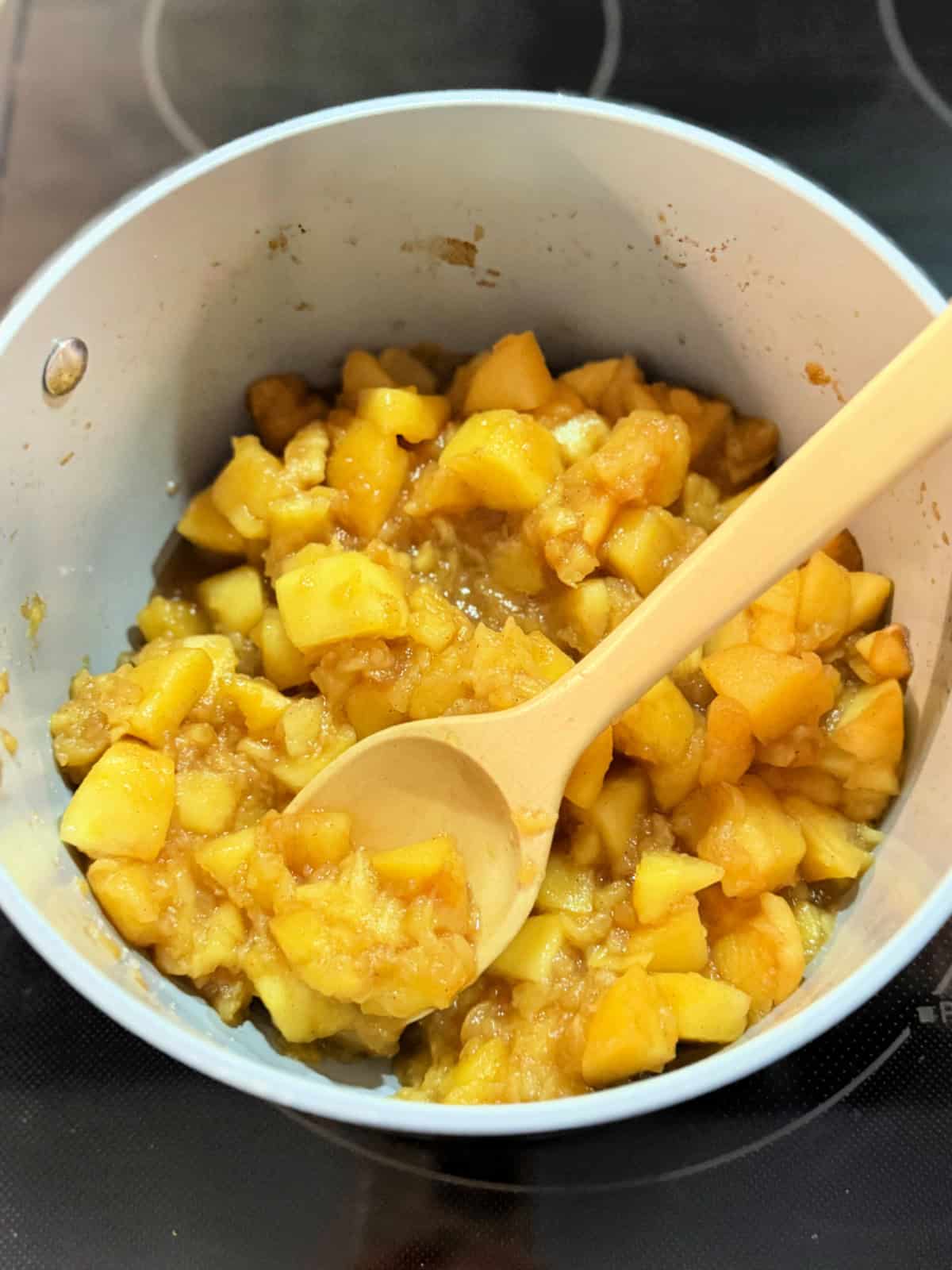 Mashed apples in sauce pot with a wooden spoon on a stove top.