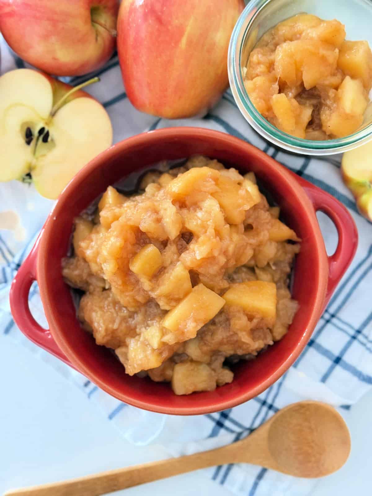 Red bowl filled with chunky applesauce and fresh apples around it.