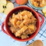 Red bowl filled with chunky applesauce on a white and blue striped towel.