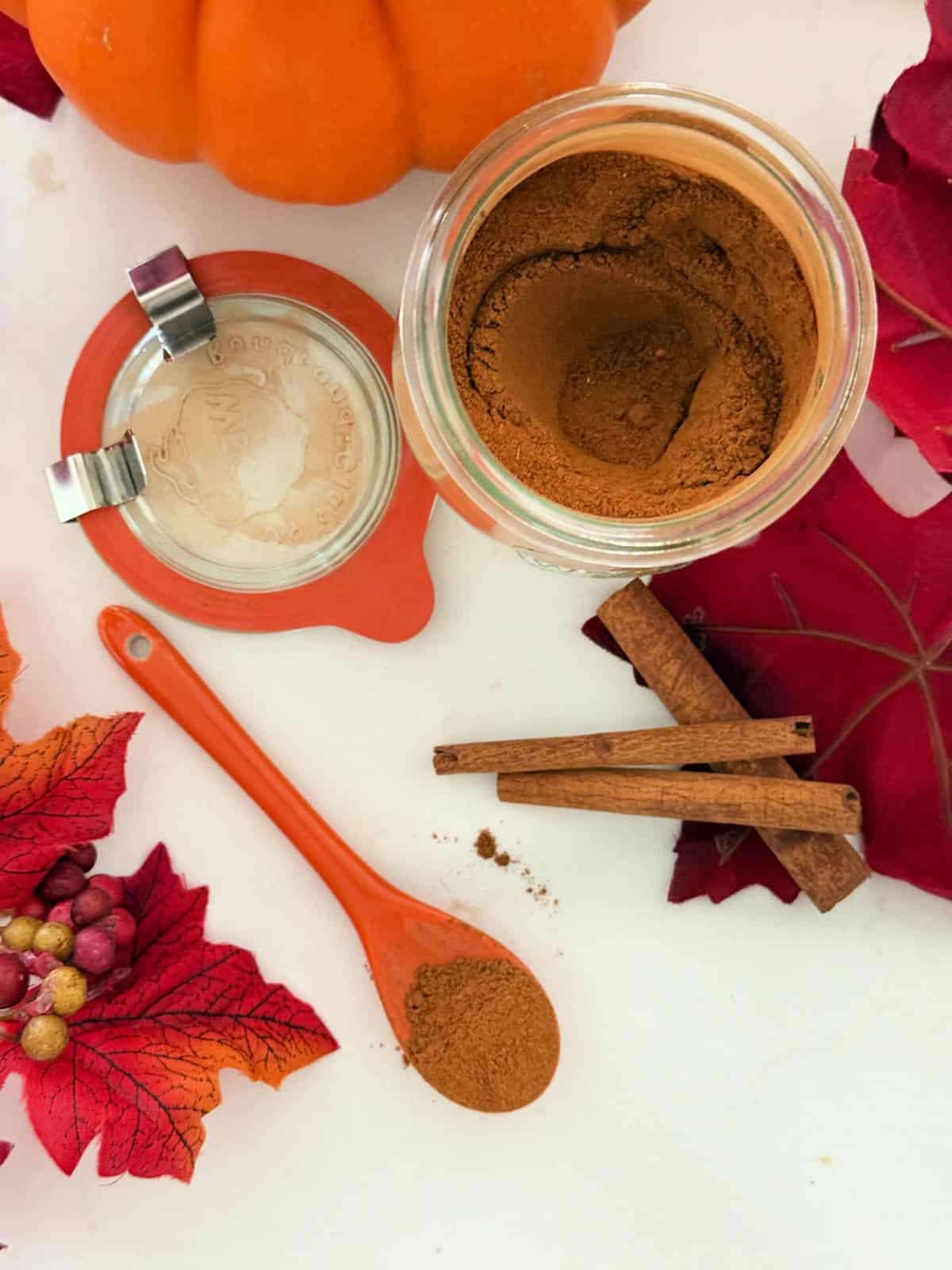 Glass jar with brown spices on a white countertop with fall leaves and pumpkins.
