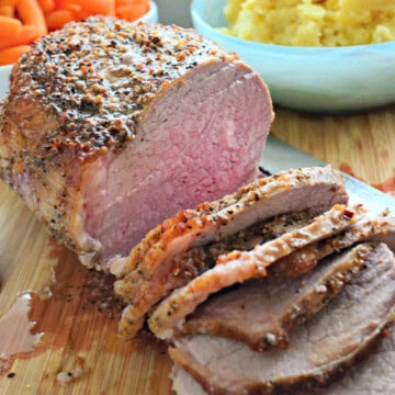Round beef on a wooden cutting board with slices off of it.
