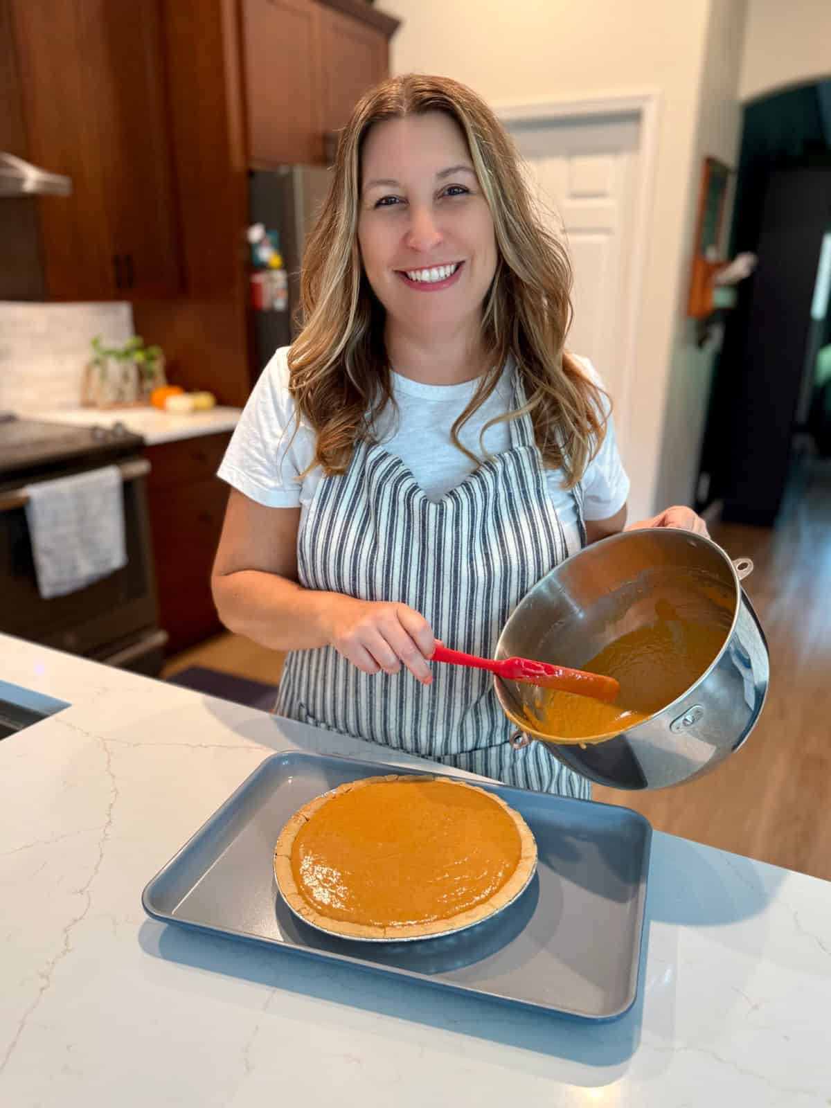 Female in a kitchen holding a metal bold and red spatula with pumpkin pie in front of her