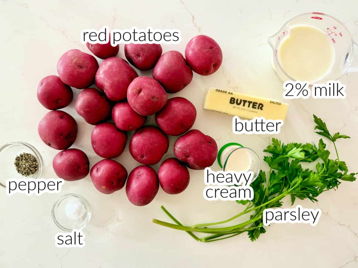 Ingredients on white counter; red potatoes, pepper, salt, butter, heavy cream, parsley, and 2% milk.
