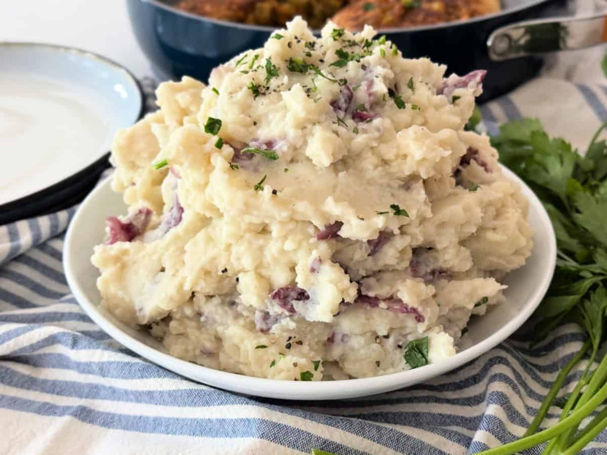 White bowl filled with mashed potatoes with red skins on a blue and white cloth.