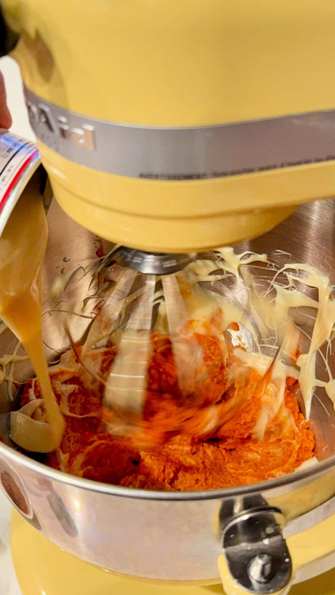 Yellow KitchenAid Mixer with condensed milk being poured into the pumpkin mix.