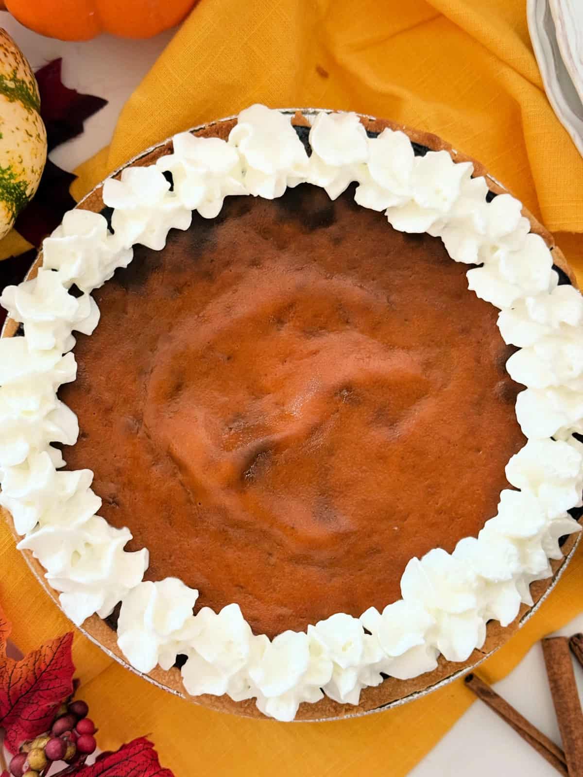 Pumpkin pie with whipped cream boarder on a yellow cloth.
