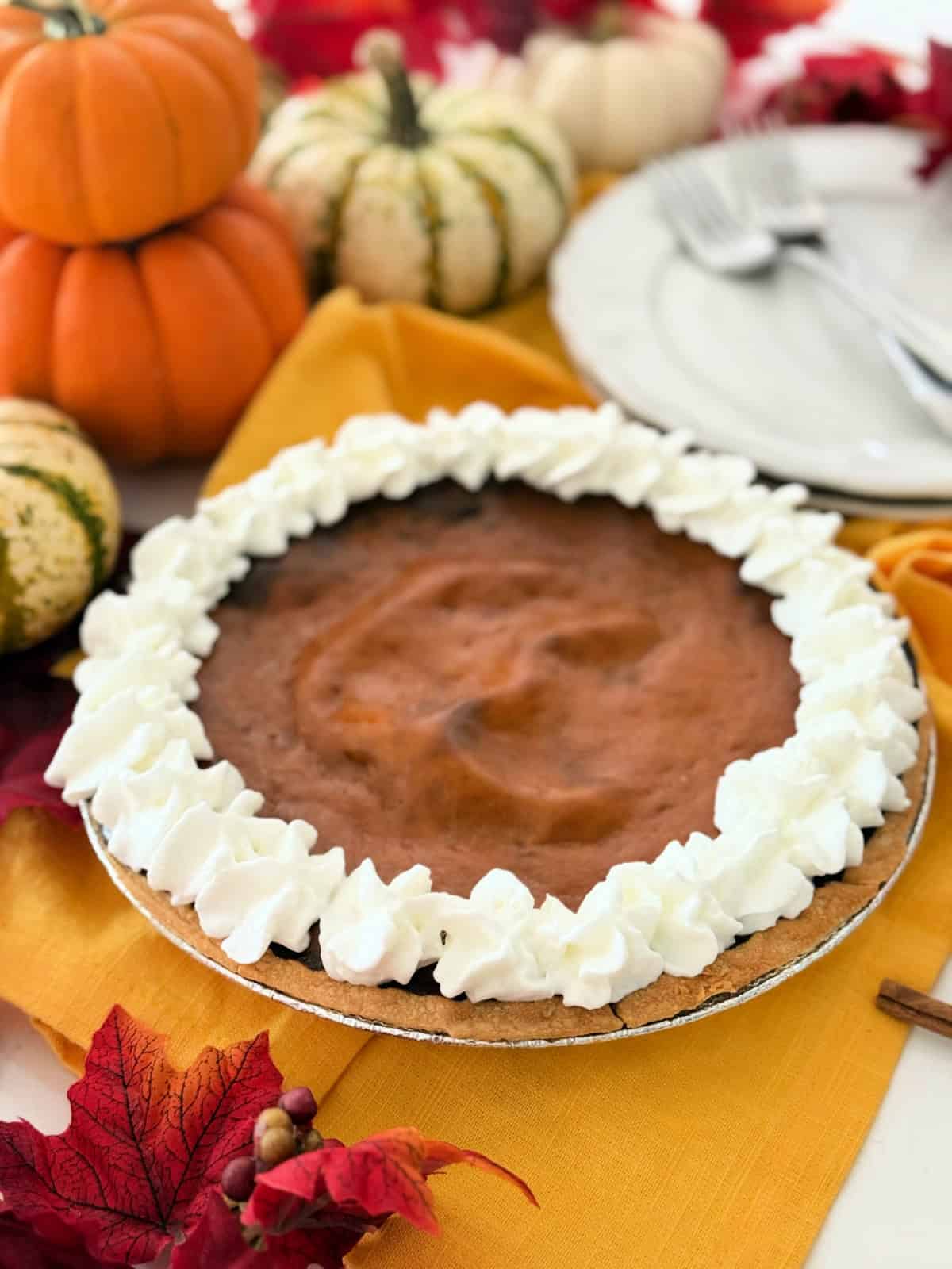 Pumpkin pie on a yellow cloth with pumpkins in background.