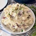 White bowl filled with mashed potatoes with red skins and topped with chopped parsley and black pepper.