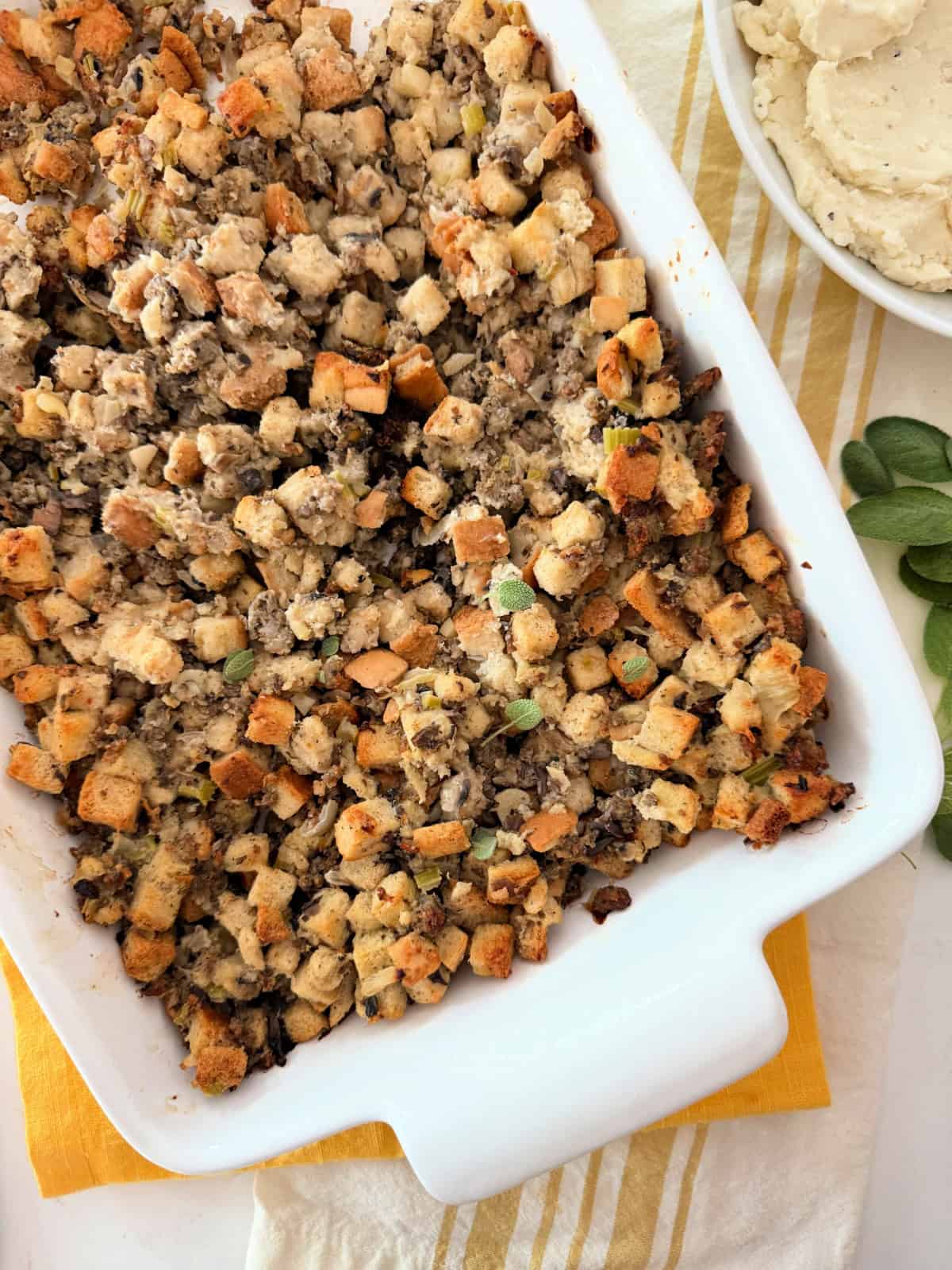Sausage stuffing in a white baking dish next to a bowl of mashed potatoes.