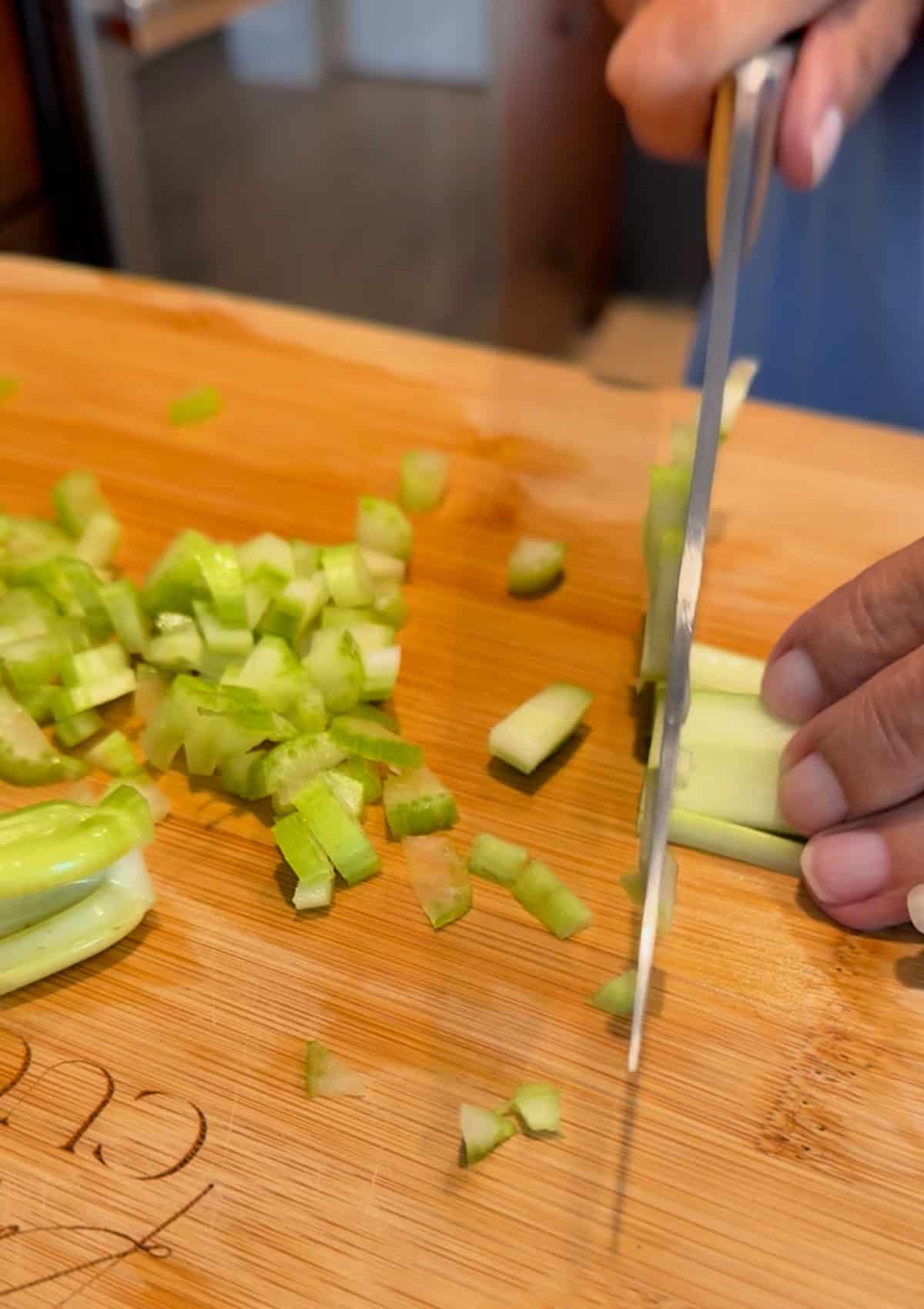 Female hand slicing celery on a wood cutting board.