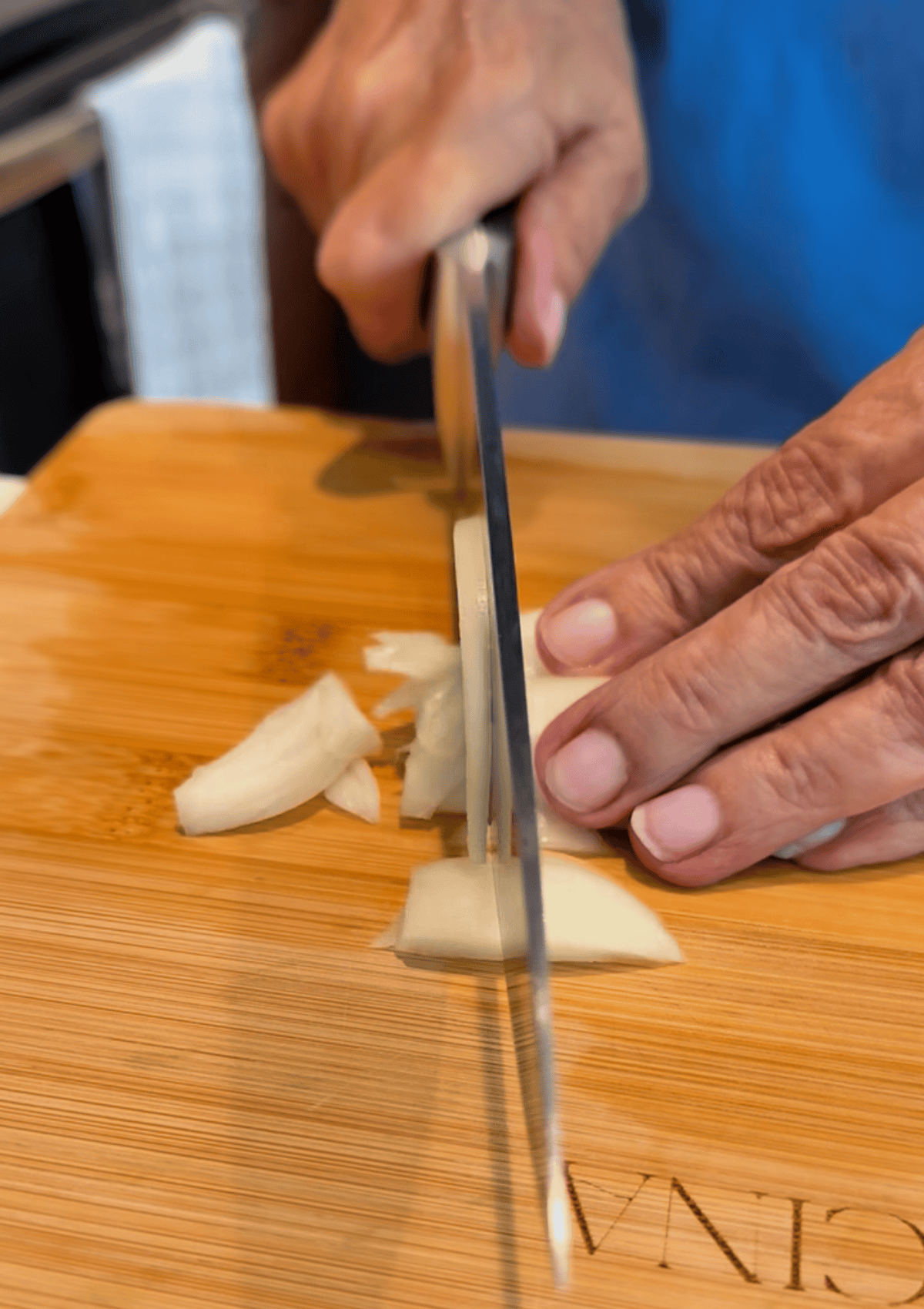 Female hand slicing an onion on a wood cutting board.