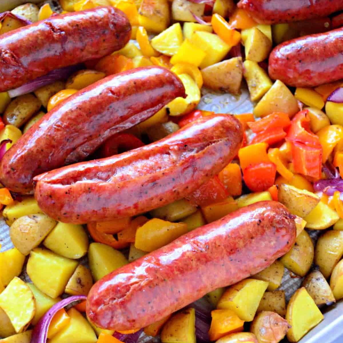 Four sausage links on a bed of potatoes and peppers layered on a sheet pan.