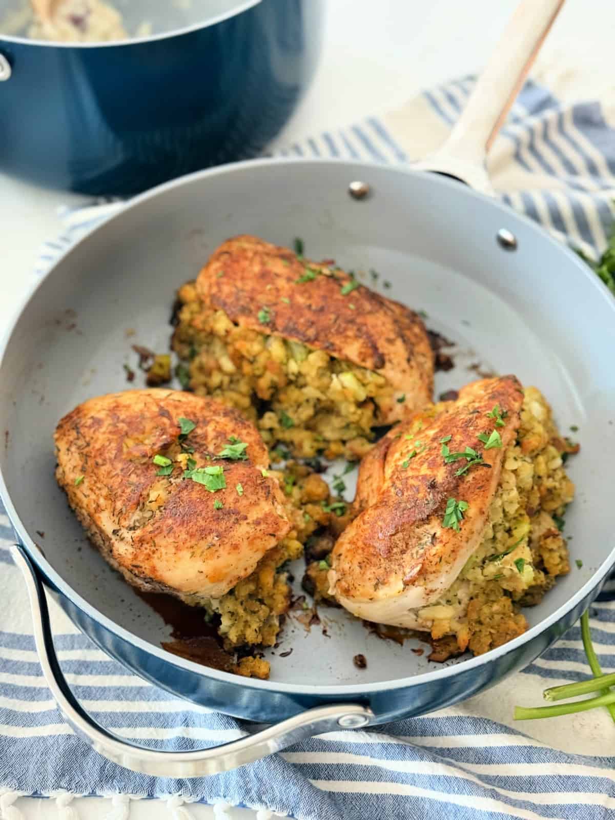 Blue frying pan filled with three roasted chicken breast split with stuffing inside them.