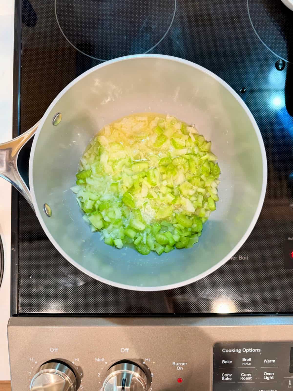 Gray pot filled with diced celery on a black stove top.