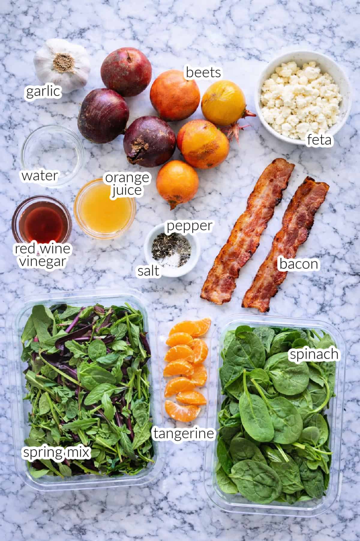 Ingredients on countertop; garlic, water, red wine vinegar, spring mix, tangerines, orange juice, salt, pepper, beets, feta, bacon, and spinach.