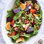 White oval dish filled with a salad with roasted beets, sliced oranges, bacon, and cheese.