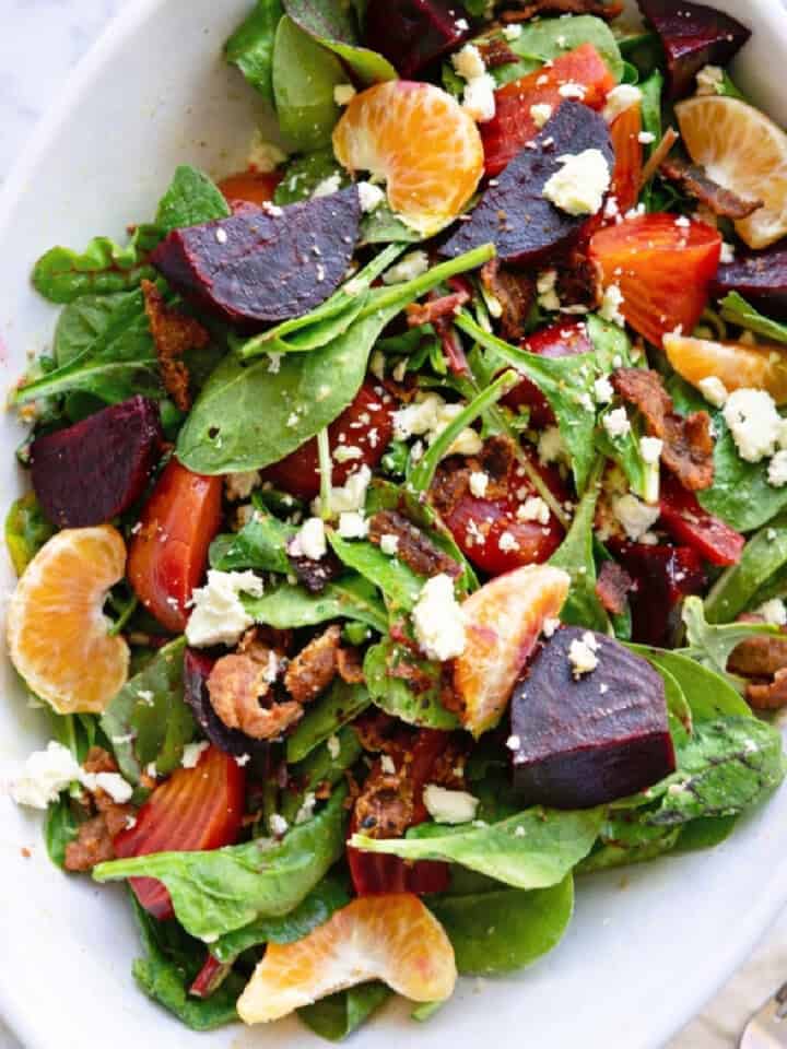 White oval dish filled with a salad with roasted beets, sliced oranges, bacon, and cheese.