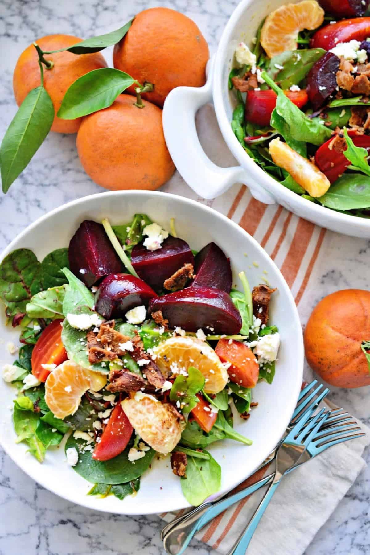 White oval dish and white circle plate filled with salad with fresh citrus scattered around the marble countertop.