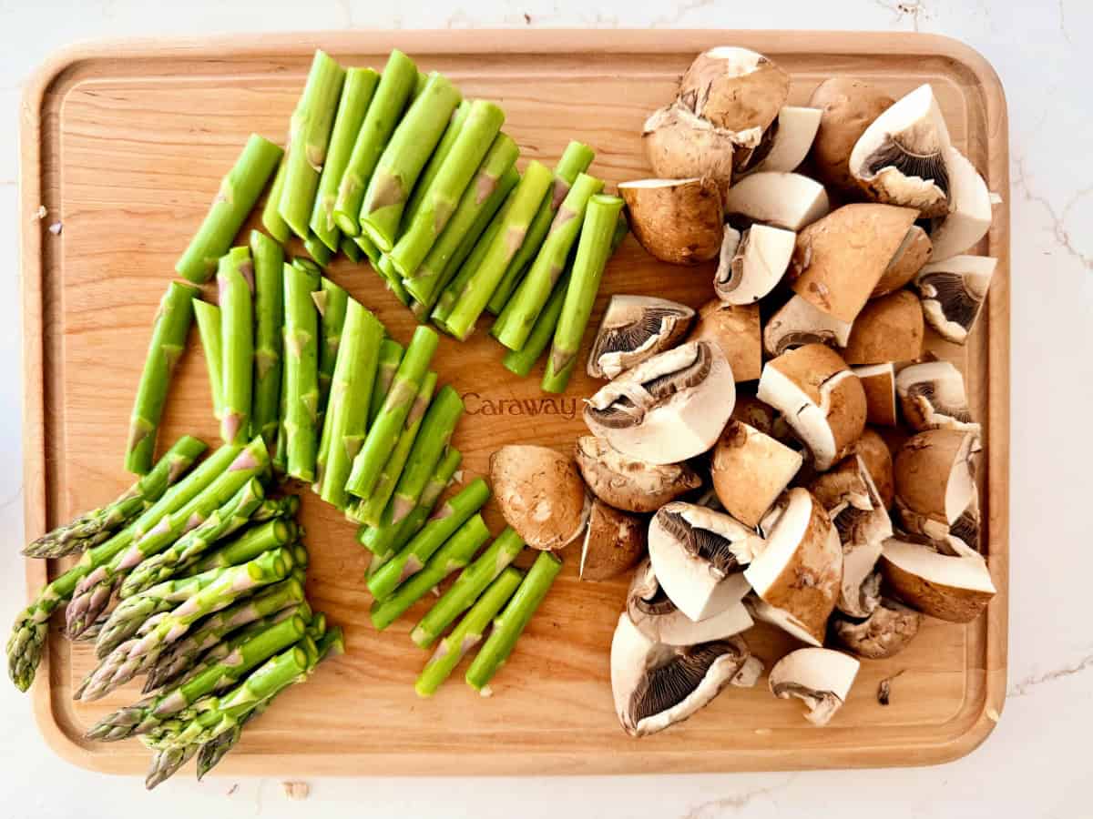 Wood cutting board with chopped asparagus, and mushrooms.