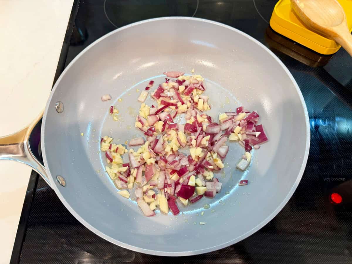 Diced red onion and garlic in a grey frying pan.